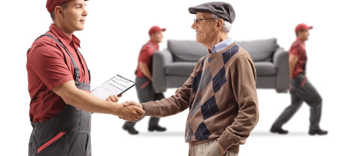 Senior man shaking hands with a mover, movers carrying a couch in the back isolated on white background